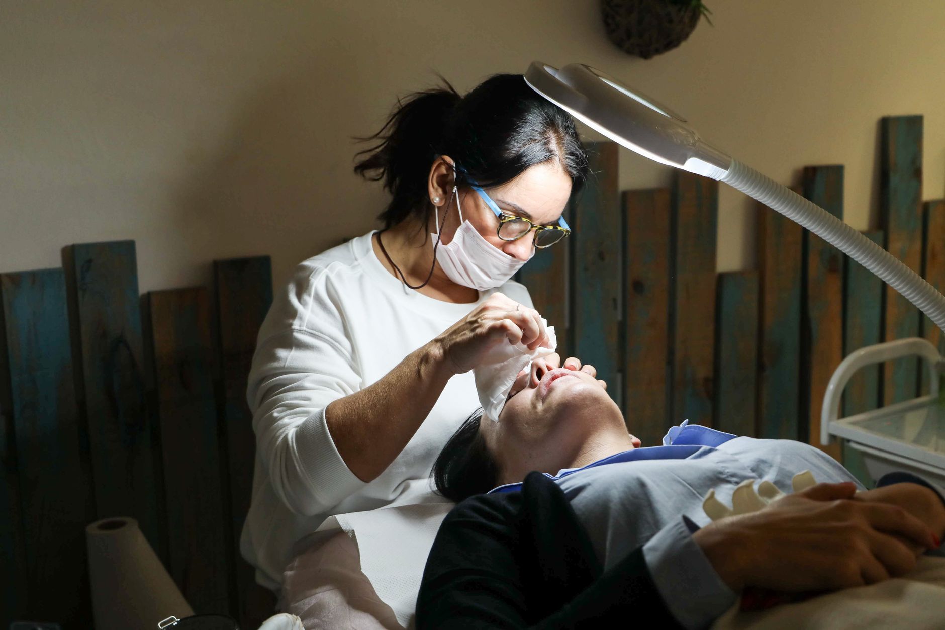esthéticienne masquée réalisant un soin du visage sous une lampe loupe