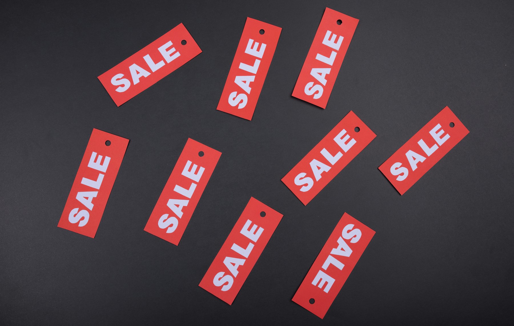 étiquettes rouges marquées SALE éparpillées sur un fond sombre, symbolisant de multiples promotions affichées