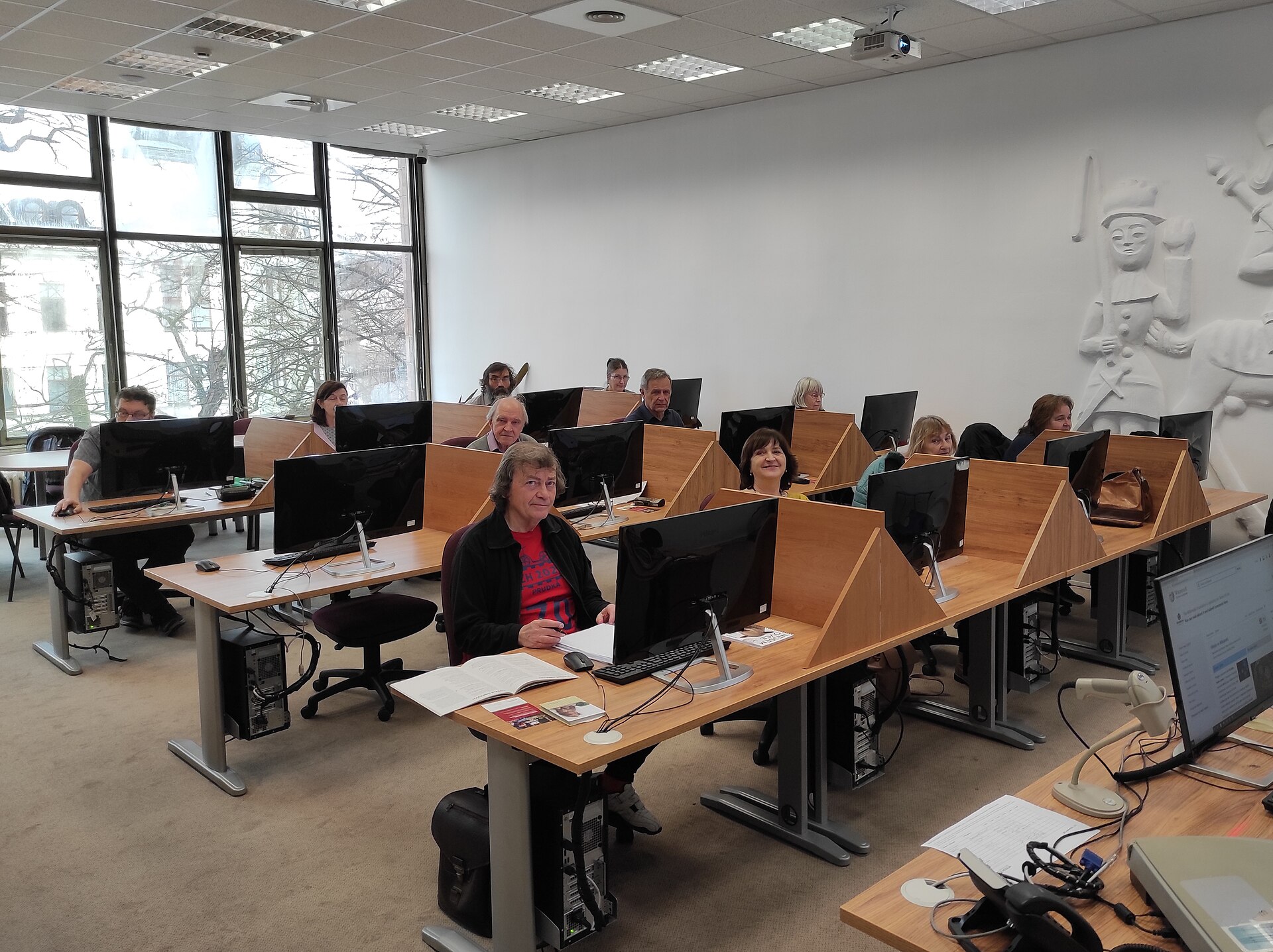 salle de cours informatique où des retraités sont assis chacun devant un ordinateur de bureau
